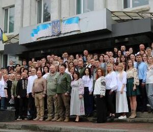 Велика група людей у вишиванках стоїть на сходах перед адміністративною будівлею з гербом України та прапорами. Колективне фото до Дня вишиванки."