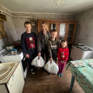 alt="Начальник служби у справах дітей з трьома дітьми стоять у кухні приватного будинку, тримаючи пакети з продуктами гуманітарної допомоги"