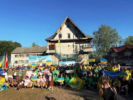 alt="Учасники Всеукраїнських спортивних змагань «Найкраща сільська спортивна громада України – 2025» під час загального фото біля адмінбудівлі в селі Ворохта. На знімку — численні команди в яскравій спортивній формі з прапорами, табличками назв громад і банерами на фоні. "