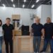 alt="група людей стоїть у приміщенні відділення поштового оператора. Перед ними — комплекти техніки у транспортних кейсах та коробках, серед яких видно дрон. Усміхнені люди — ймовірно, представники громади та працівники відділення."