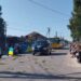 Прощальна церемонія у селі: люди стоять і сидять на колінах обабіч дороги, вшановуючи загиблого Захисника. Посеред вулиці — катафалк, прикрашений квітами, попереду — державний прапор України, люди з прапорами та квітами. На дорозі розкидані зелені гілки. Атмосфера скорботи та поваги
