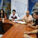 На знімку — учасники онлайн-наради за великим дерев’яним столом. Перед ними документи, ноутбуки та монітор. У центрі — жінка в білій сорочці та бордовому жилеті, поруч сидять чоловіки та жінка.