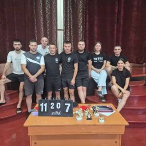 Групове фото учасників турніру з настільного тенісу серед ветеранів та ВПО в Будинку культури села Городок. Спортсмени та організатори заходу позують біля столу з кубками, медалями та рахунковою табло.