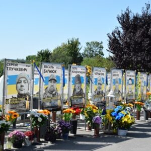 На світлині – меморіальна стіна з портретами загиблих Захисників України у Городку. Перед стендами встановлені численні квіти та лампадки на знак пам’яті та вдячності Героям