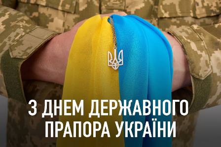 Військовослужбовець у камуфляжній формі тримає у руках жовто-блакитну тканину, на якій висить підвіска у вигляді тризуба — герба України. Внизу зображення напис: «З Днем Державного Прапора України».