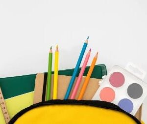 «Жовтий рюкзак із канцелярським приладдям: зошити, лінійка, кольорові олівці та акварельні фарби на білому фоні»