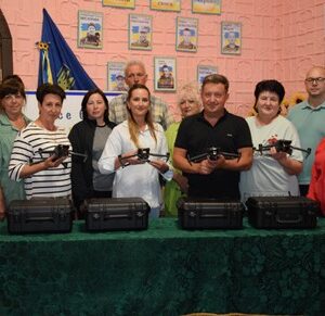 Група представників Городоцької громади під час передачі дронів «Mavic 3T» для військових: на столі розміщені комплекти у кейсах, кілька людей тримають у руках дрони