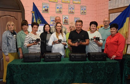 Група представників Городоцької громади під час передачі дронів «Mavic 3T» для військових: на столі розміщені комплекти у кейсах, кілька людей тримають у руках дрони