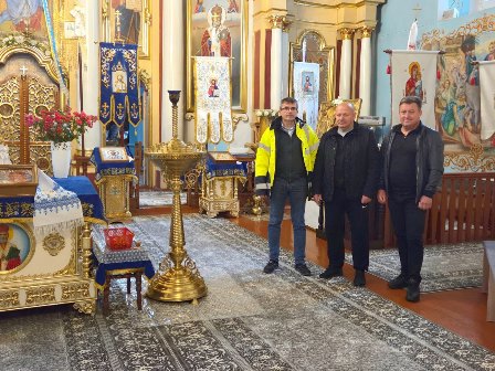 Троє чоловіків стоять у відремонтованому Свято-Миколаївському храмі у Городку. На передньому плані видно нове килимове покриття, ікони та церковне оздоблення. На задньому плані — іконостас та розписані стіни храму.