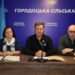 На зображенні троє представників Городоцької сільської ради сидять за столом під час засідання. Посередині — сільський голова, поруч із ним – працівники ради. На стіні позаду розміщено синє тло з написом «Городоцька сільська рада» та державним прапором України.