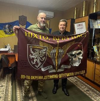 На фото представник 80-ї окремої десантно-штурмової бригади Збройних Сил України передає прапор бригади та Подяку голові Городоцької сільської ради Сергію Поліщуку. Обидва чоловіки тримають прапор із написом «Ніхто, крім нас!»