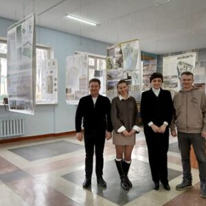 У вестибюлі навчального корпусу НУВГП чотири учасники заходу позують на фоні виставки студентських архітектурних проєктів — планшети з концепціями громадського простору підвішені та розміщені навколо експозиційного простору.