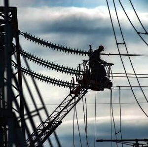 Електромонтер виконує роботи на лініях електропередачі з використанням автовишки на фоні неба.