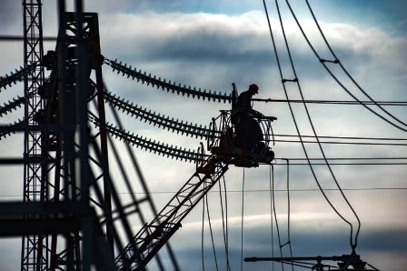 Електромонтер виконує роботи на лініях електропередачі з використанням автовишки на фоні неба.