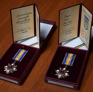 Дві державні нагороди України у відкритих футлярах із посвідченнями та синьо-жовтими стрічками, розміщені на дерев’яній поверхні.