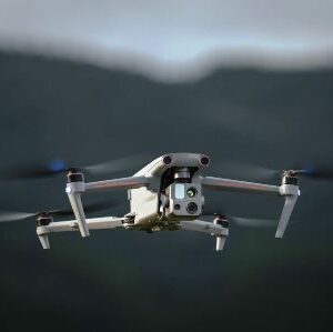 Квадрокоптерний дрон із камерою на підвісі летить у повітрі на тлі розмитих гір і неба, знятий крупним планом спереду