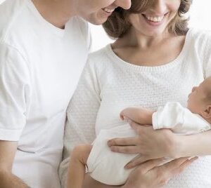 Молода сім’я тримає на руках новонароджену дитину та усміхається.