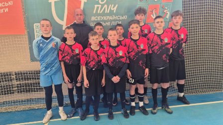 Групове фото юної футбольної команди «Тигри» у спортивній формі: хлопці стоять у залі перед сіткою та банером «Пліч-о-пліч всеукраїнські шкільні ліги», поруч тренер і воротар у формі.