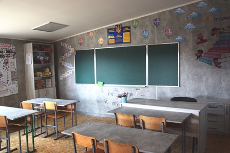 Оновлений клас із зеленою дошкою, партами та навчальними матеріалами на стінах у шкільному кабінеті.