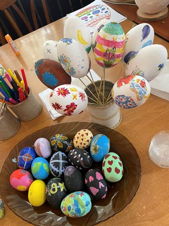 На фото — святково оформлена композиція з писанками. На дерев’яному столі стоїть скляна банка з декоративними яйцями на паличках, розписаними яскравими візерунками: квітами, смужками та орнаментами.
