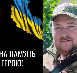 Меморіальне зображення: ліворуч палаюча свічка на темному тлі поруч із синьо-жовтим прапором України та написом “Вічна пам’ять”; праворуч — портрет чоловіка у військовому одязі та кепці на фоні зелені; внизу — символічний ланцюг як знак скорботи та втрати