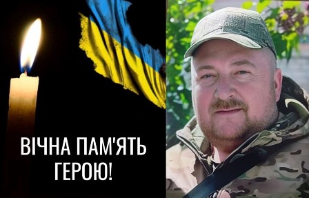 Меморіальне зображення: ліворуч палаюча свічка на темному тлі поруч із синьо-жовтим прапором України та написом “Вічна пам’ять”; праворуч — портрет чоловіка у військовому одязі та кепці на фоні зелені; внизу — символічний ланцюг як знак скорботи та втрати