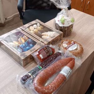 Набір продуктів на столі: ковбаси, солодощі в коробках, випічки і Паска в упаковці.