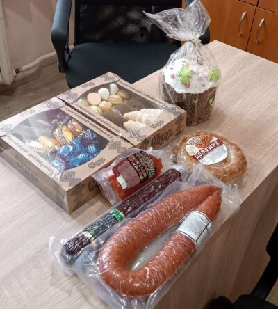 Набір продуктів на столі: ковбаси, солодощі в коробках, випічки і Паска в упаковці.