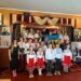 Групове фото учасників благодійного заходу «Вишийте матусю, вишиванку» у будинку культури села Карпилівка. Діти та дорослі у традиційних українських вишиванках позують на сцені з державним прапором України.