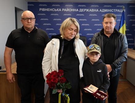 Родина загиблого Захисника України під час церемонії вручення ордена «За мужність» ІІІ ступеня (посмертно) у Рівненській районній державній адміністрації. Дружина та син Героя тримають державну нагороду і квіти, поруч — представники влади Городоцької громади та Рівненського району.