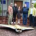 П’ятеро людей стоять біля входу до адміністративної будівлі поруч із фрагментом знешкодженого ворожого дрона «Герань», розміщеного на бруківці.