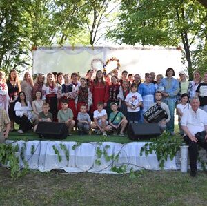 Групове фото учасників творчого заходу на сцені просто неба в парковій зоні серед дерев.