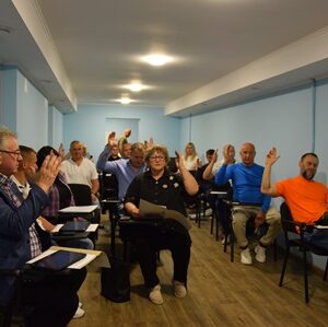 Учасники засідання Городоцької сільської ради голосують за порядок денний у залі засідань. Депутати сидять за столами, піднявши руки під час прийняття рішення.