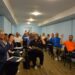 Учасники засідання Городоцької сільської ради голосують за порядок денний у залі засідань. Депутати сидять за столами, піднявши руки під час прийняття рішення.