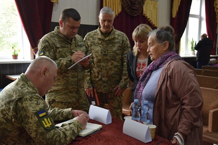 Військовослужбовці спілкуються з жінками під час зустрічі у залі засідань, один із військових записує звернення у блокнот.
