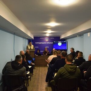 У залі засідань відбувається сесія сільської ради: попереду за столом сидять представники керівництва громади, один із них виступає з доповіддю.