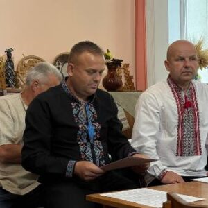 Члени виконавчого комітету під час засідання Городоцької сільської ради: чоловіки у традиційних українських вишиванках та діловому одязі працюють із документами за столом у залі засідань.
