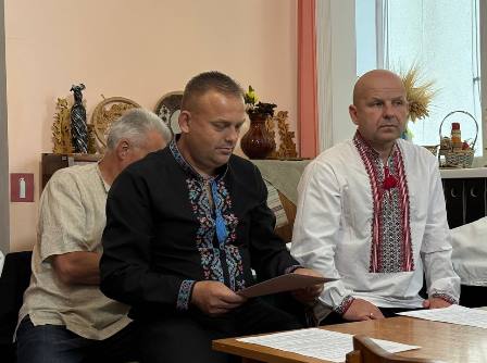 Члени виконавчого комітету під час засідання Городоцької сільської ради: чоловіки у традиційних українських вишиванках та діловому одязі працюють із документами за столом у залі засідань.