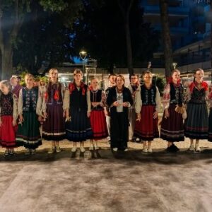 Група жінок і дівчат у традиційному українському вбранні стоїть у ряд на вечірньому майданчику серед дерев.