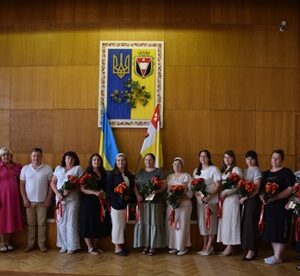 У великій залі Рівненської районної державної адміністрації на тлі державної символіки України та прапорів група жінок стоїть для спільного фото після урочистого вручення почесних звань «Мати-героїня».