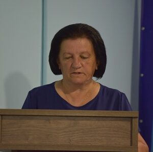 Жінка виступає за дерев'яною трибуною під час засідання Городоцької сільської ради. Праворуч видно прапор України.