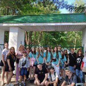 Група дітей та підлітків разом із супроводжуючими позують для спільного фото біля входу на територію оздоровчого або туристичного комплексу