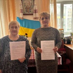 Дві жінки стоять в офісі та тримають підписані документи після укладення меморандуму про співпрацю.