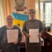 Дві жінки стоять в офісі та тримають підписані документи після укладення меморандуму про співпрацю.