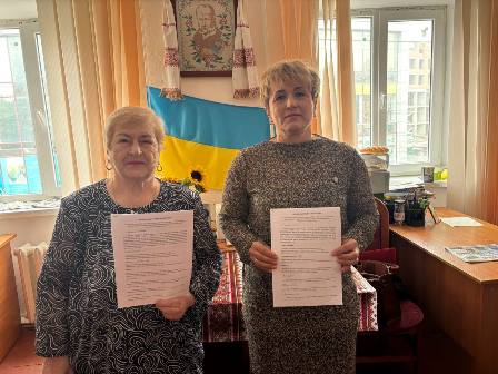 Дві жінки стоять в офісі та тримають підписані документи після укладення меморандуму про співпрацю.