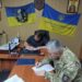 У службовому кабінеті за столом сидять двоє чоловіків — один у цивільному одязі, інший у військовій формі — та підписують документи про співпрацю.