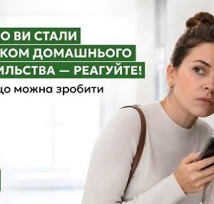 Жінка у світлому одязі стоїть біля стіни, тримаючи в руці смартфон і насторожено прислухаючись.