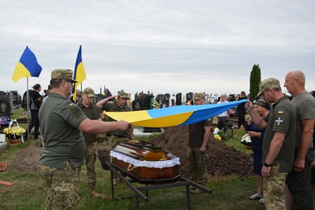 Військовослужбовці під час церемонії поховання тримають над труною загиблого Захисника України синьо-жовтий Державний Прапор.