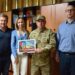Четверо людей стоять в службовому кабінеті. У центрі — військовослужбовець у камуфляжній формі, який тримає в руках подяку в рамці.