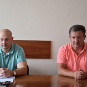 Двоє чоловіків у світлих футболках-поло сидять за столом під час робочої наради в адміністративному приміщенні.